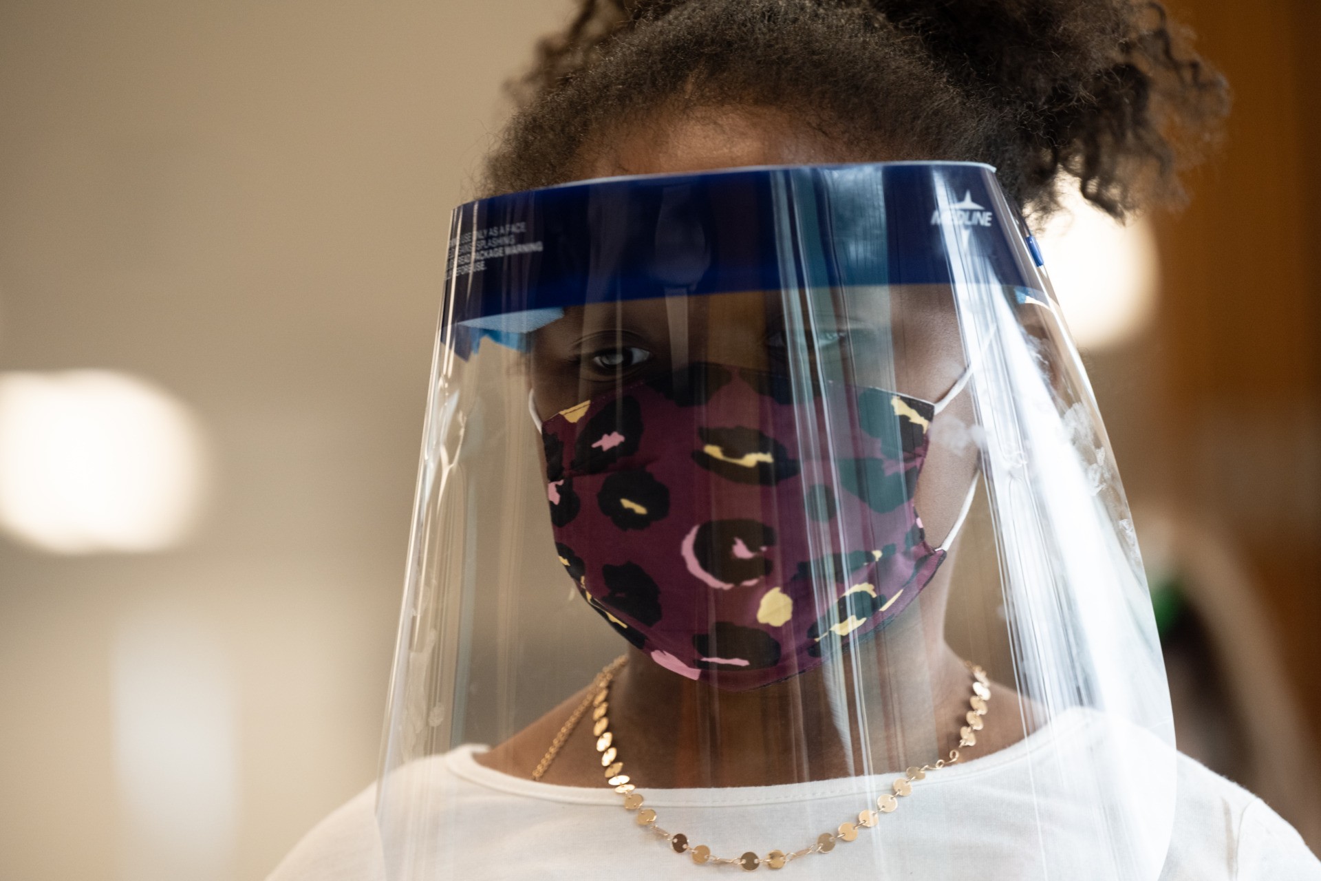 LOUISVILLE, KY - MARCH 17: A child wearing a face shield and mask stands in the cafeteria of Medora Elementary School on March 17, 2021 in Louisville, Kentucky. Today marks the reopening of Jefferson County Public Schools for in-person learning with new COVID-19 procedures in place. (Photo by Jon Cherry/Getty Images)
