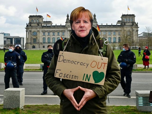 A protestor wearing a mask depicting German Chancellor Angela Merkel takes part in a demon
