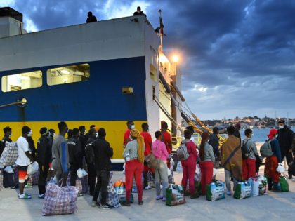 Migrants from a migrant housing centre on the Italian island of Lampedusa, are guided by a security official on May 14, 2021, as they prepare to board the ship 'Cossyra', bound for the Sicilian town of Porto Empedocle. - Migration has returned to the top of the political agenda in …
