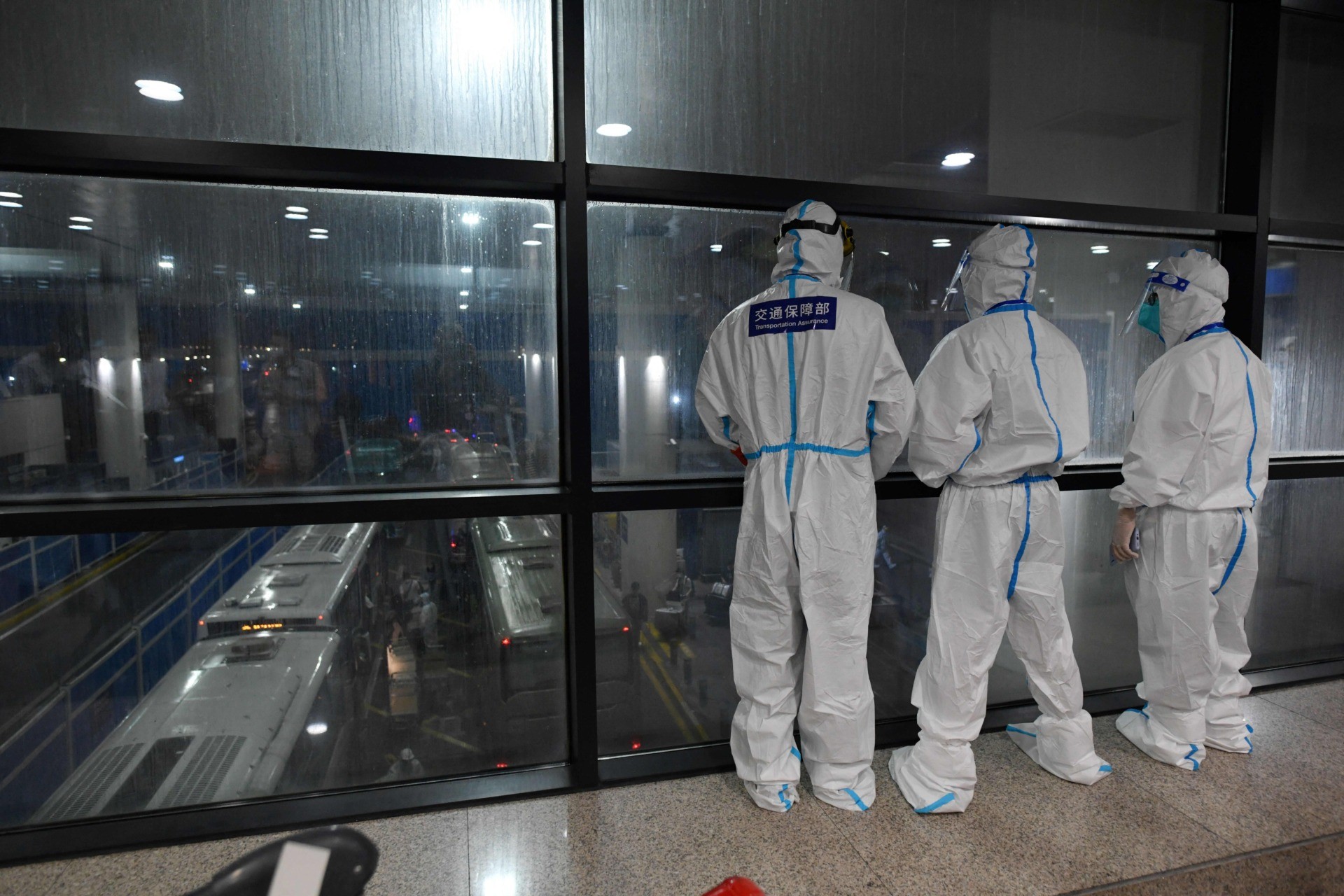 Workers in protective clothing as a precaution against the Covid-19 coronavirus watch over arriving international passengers as they board buses to be taken to quarantine hotels, at Pudong airport in Shanghai on August 13, 2021. (Photo by GREG BAKER / AFP) (Photo by GREG BAKER/AFP via Getty Images)