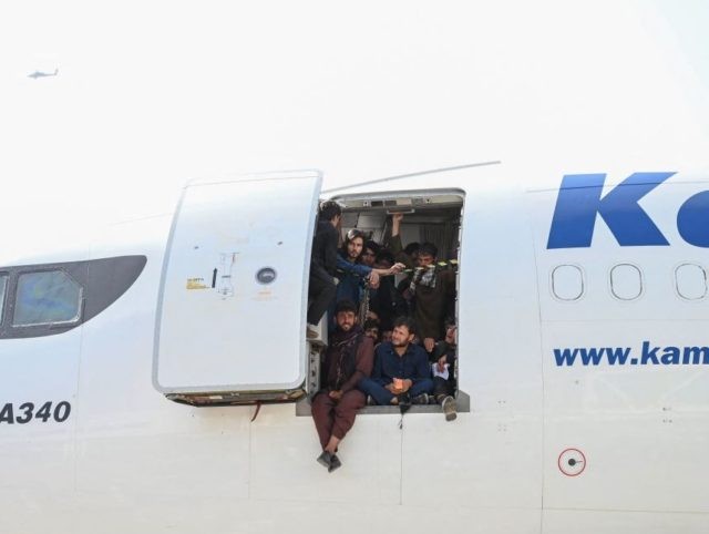 TOPSHOT - Afghan people climb up on a plane and sit by the door as they wait at the Kabul airport in Kabul on August 16, 2021, after a stunningly swift end to Afghanistan's 20-year war, as thousands of people mobbed the city's airport trying to flee the group's feared …
