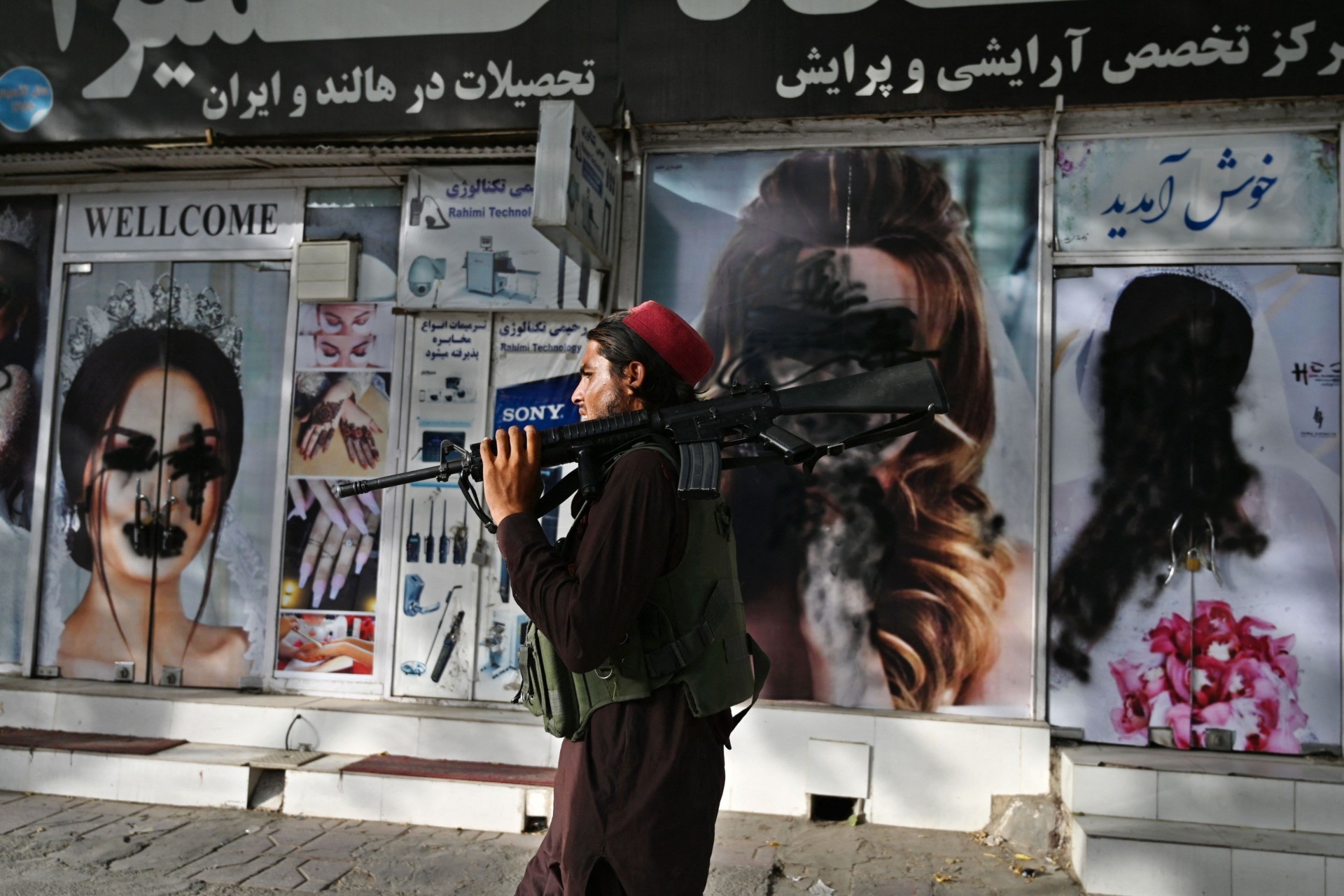 TOPSHOT - A Taliban fighter walks past a beauty salon with images of women defaced using spray paint in Shar-e-Naw in Kabul on August 18, 2021. (Photo by Wakil KOHSAR / AFP) (Photo by WAKIL KOHSAR/AFP via Getty Images)