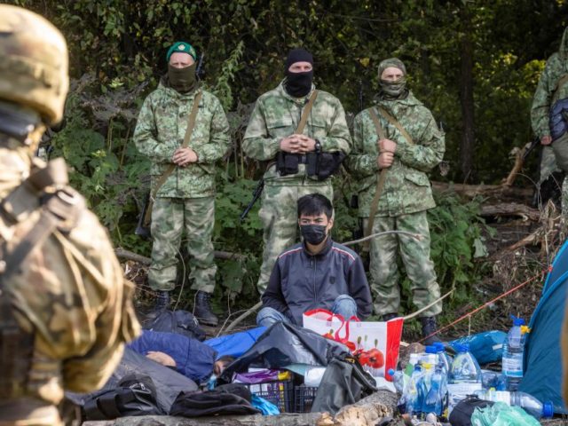 Polish (front) and Belarusian border guards (background) stand next to a group of migrants