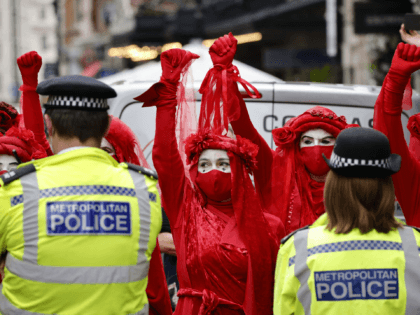 Members of the Red Rebel Brigade - an international performance artivist troupe - face a cordon of police officers as they join climate activists from the Extinction Rebellion group in central London on August 23, 2021 as the group launched its 'Impossible Rebellion' series of actions. - Thousands of climate …