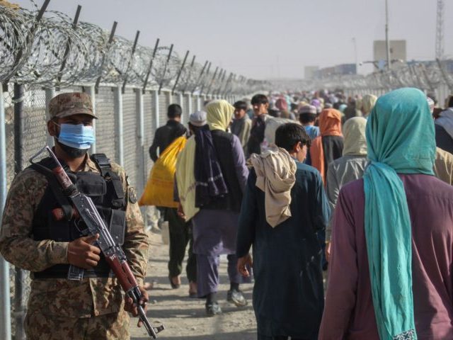 A Pakistani soldier stands guard as Afghans walk along fences after arriving in Pakistan t