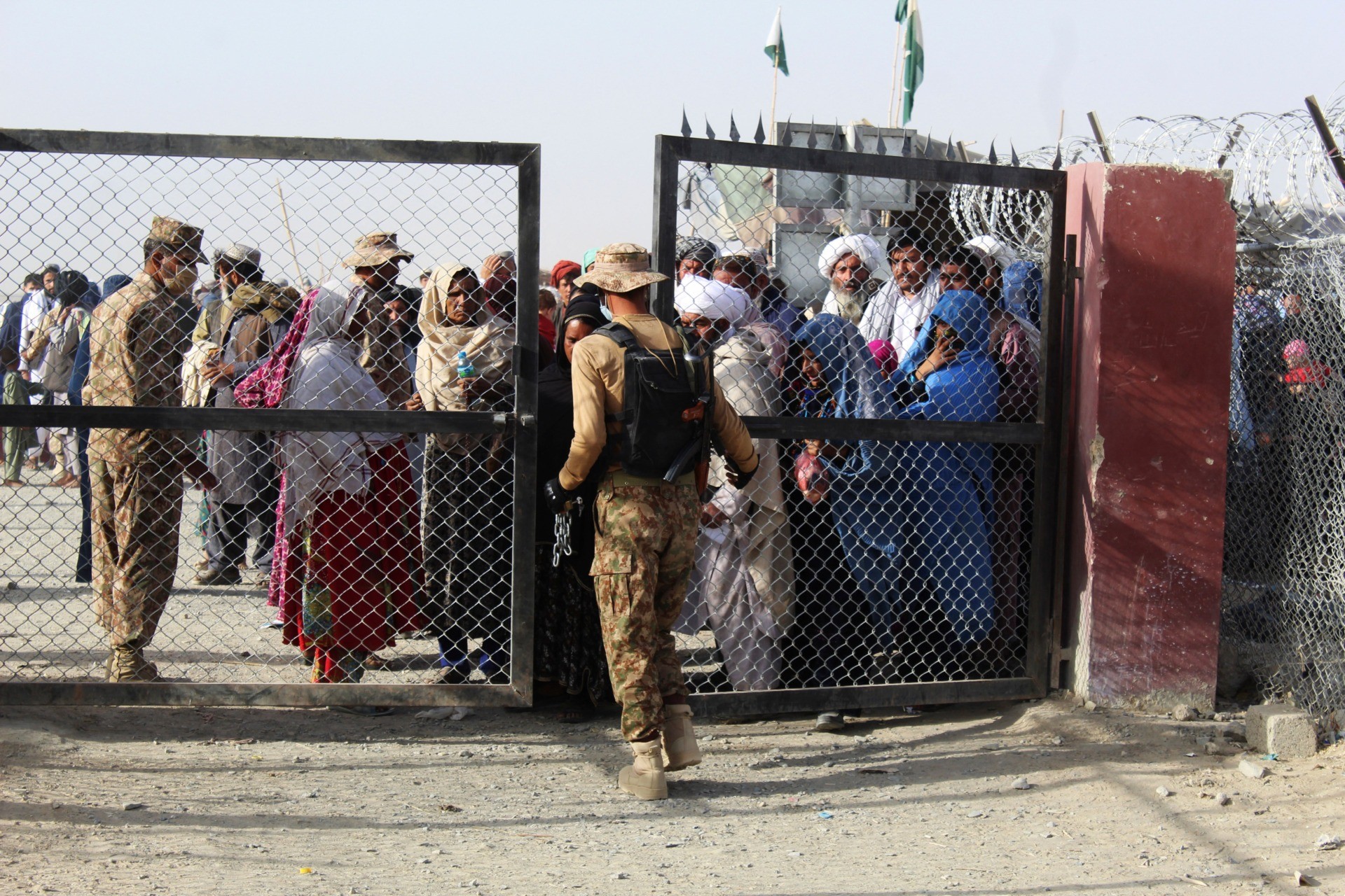 A Pakistani soldier holds a gate as Afghan and Pakistani people wait to enter Afghanistan through the Pakistan-Afghanistan border crossing point in Chaman on August 27, 2021 following the Taliban's stunning military takeover of Afghanistan. (Photo by - / AFP) / The erroneous mention[s] appearing in the metadata of this photo by - has been modified in AFP systems in the following manner: [to enter Afghanistan] instead of [to enter Pakistan]. Please immediately remove the erroneous mention[s] from all your online services and delete it (them) from your servers. If you have been authorized by AFP to distribute it (them) to third parties, please ensure that the same actions are carried out by them. Failure to promptly comply with these instructions will entail liability on your part for any continued or post notification usage. Therefore we thank you very much for all your attention and prompt action. We are sorry for the inconvenience this notification may cause and remain at your disposal for any further information you may require. (Photo by -/AFP via Getty Images)