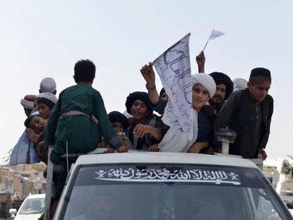 TOPSHOT - Youths supporting the Taliban wave Taliban flags atop a vehicle while marching w