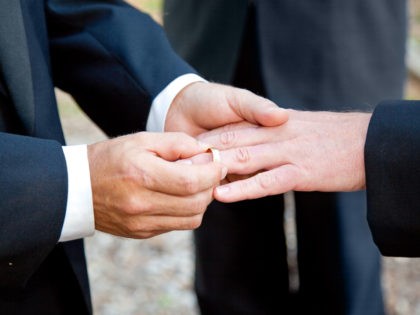 One groom placing the ring on another man's finger during gay wedding.