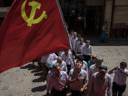 KASHGAR, CHINA - JUNE 30: Ethnic Uyghur members of the Communist Party of China carry a flag as they take part in an organized tour on June 30, 2017 in the old town of Kashgar, in the far western Xinjiang province, China. Kashgar has long been considered the cultural heart …