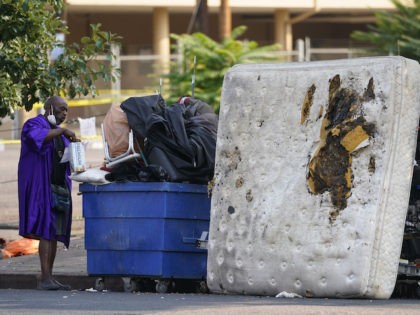 A man opens up a box of saltine crackers while waiting with his belongings to be cleared during a homeless sweep by the cioty of Denver near the corner of 22nd and Champa Tuesday, Aug. 25, 2020, north of downtown Denver. (AP Photo/David Zalubowski)