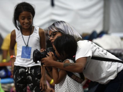 A photographer shows a migrant girl how to use her camera, at a stadium-turned-shelter in Mexico City, where Central American migrants - mostly Hondurans- who are taking part in a caravan towards the US, rest during a stop in their journey, on November 6, 2018. - A caravan of Central …