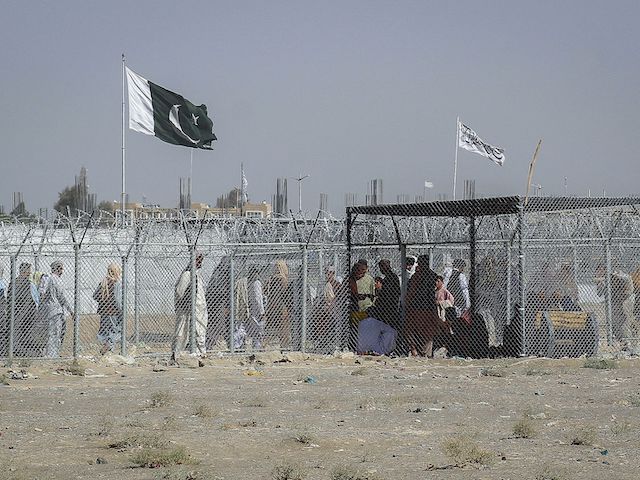 Afghan and Pakistani nationals walk through a security barrier to cross the border as a national flag of Pakistan and a Taliban flag is masted in the Pakistan-Afghanistan border crossing point in Chaman on August 24, 2021, following Taliban's military takeover of Afghanistan. (Photo by - / AFP) (Photo by -/AFP via Getty Images)