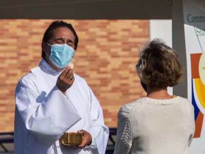 A priest wearing a facemask gives Communion to a woman at an outdoor Sunday service at Saints Simon & Jude Catholic Church in Huntington Beach, California, on July 19, 2020. - Given the increase in COVID-19 cases in the state of California and the mask's controversy in the US, where …