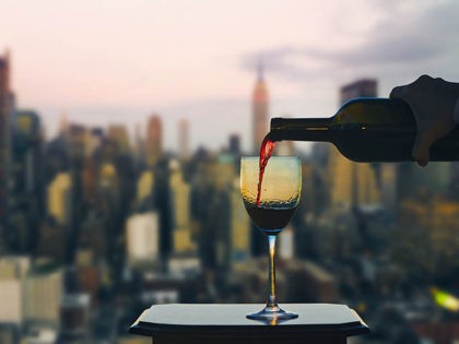 Female hand with bottle pours red wine into glasses on Manhattan background. New York city