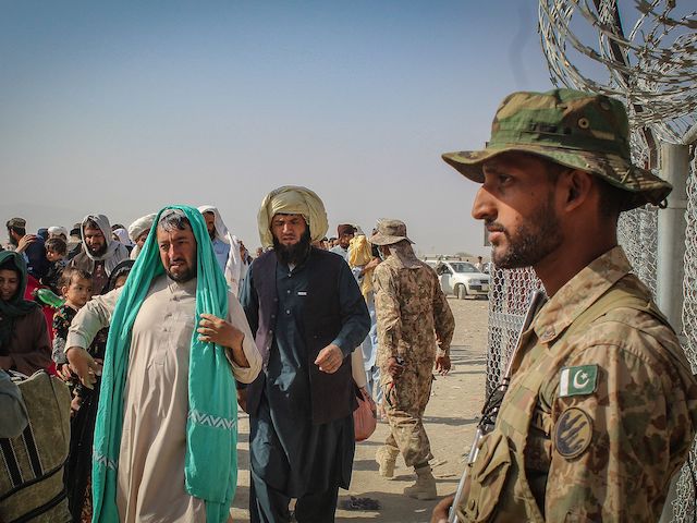 A Pakistani soldier (R) stands guard as Afghan nationals arrive at the Pakistan-Afghanistan border crossing point in Chaman on August 19, 2021 to return back to Afghanistan. (Photo by - / AFP) (Photo by -/AFP via Getty Images)