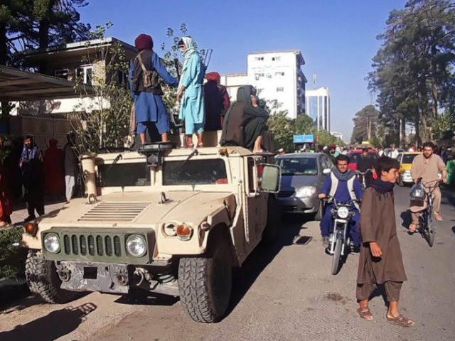 In this picture taken on August 13, 2021, Taliban fighters stand on a vehicle along the ro