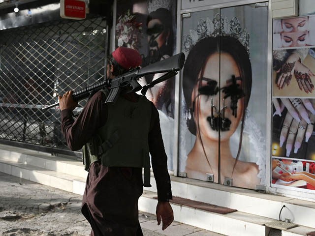 A Taliban fighter walks past a beauty salon with images of women defaced using spray paint