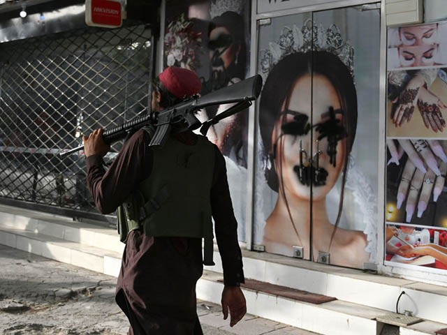 A Taliban fighter walks past a beauty salon with images of women defaced using spray paint in Shar-e-Naw in Kabul on August 18, 2021. (Photo by Wakil KOHSAR / AFP) (Photo by WAKIL KOHSAR/AFP via Getty Images)