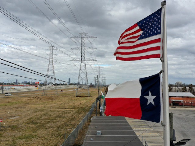 HOUSTON, TEXAS - FEBRUARY 21: The U.S. and Texas flags fly in front of high voltage transm