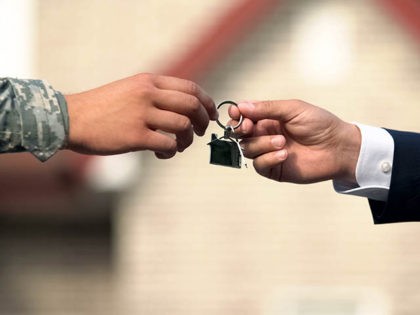 Man in business suit giving house key to man in military uniform, state support