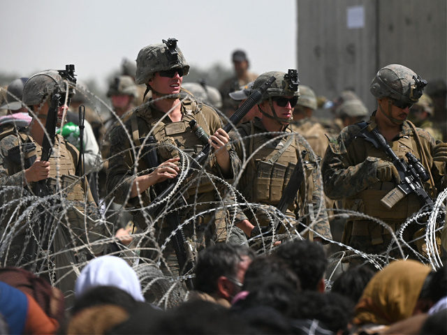 US soldiers stand guard behind barbed wire as Afghans sit on a roadside near the military