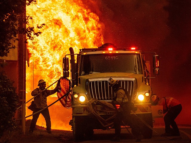 TOPSHOT - A firefighter saves an American flag as flames consume a home during the Dixie fire in Greenville, California on August 4, 2021. - The Dixie fire burned through dozens of homes and businesses in downtown Greenville and continues to forge towards other residential communities. Officials in northern California on August 4, 2021 warned residents of two communities in the path of the raging Dixie fire to evacuate immediately as high winds whipped the flames onwards. (Photo by Josh Edelson / AFP) (Photo by JOSH EDELSON/AFP via Getty Images)