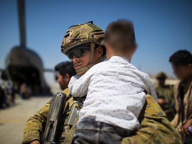 An Australian Army soldier, part of the 1st Battalion, Royal Australian Regiment ready combat team carries an Afghan child while assisting a family aboard the RAAF C-17A Globemaster at the Hamid Karzai International Airport.