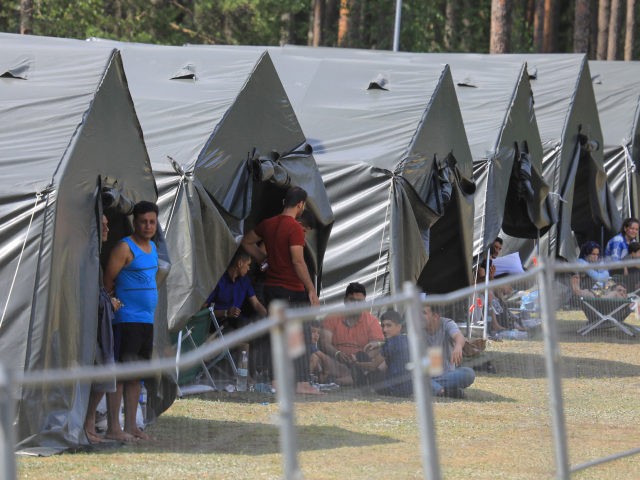 Migrants are seen through a fence as they stand and sit by tents in a camp near the border