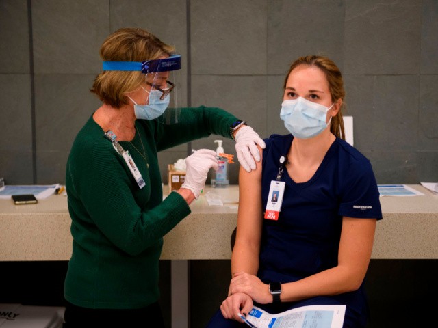 Traveling registered nurse Taylor Reed (R) receives a Covid-19 vaccination at Martin Luther King Jr. (MLK) Community Hospital on January 6, 2021 in the Willowbrook neighborhood of Los Angeles, California. - Deep within a South Los Angeles hospital, a row of elderly Hispanic men in induced comas lay hooked up to ventilators, while nurses clad in spacesuit-looking respirators checked their bleeping monitors in the eerie silence. The intensive care unit in one of the city's poorest districts is well accustomed to death, but with Los Angeles now at the heart of the United States' Covid pandemic, medics say they have never seen anything on this scale. (Photo by Patrick T. FALLON / AFP) (Photo by PATRICK T. FALLON/AFP via Getty Images)