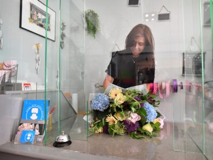 Florist Trish Collins-Morgan works behind a plastic screen as she re-opens her shop, with