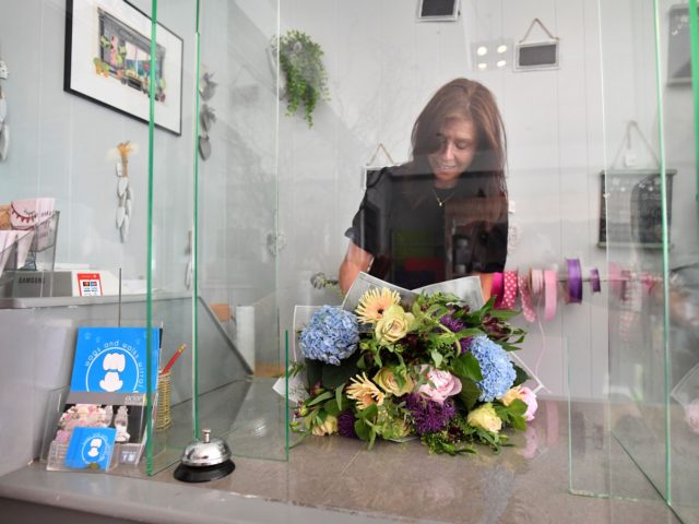 Florist Trish Collins-Morgan works behind a plastic screen as she re-opens her shop, with various safety policies in place, in West Kirby north west England on June 17, 2020, as lockdown restrictions are eased during the novel coronavirus COVID-19 pandemic. - Various stores and outdoor attractions in England opened Monday …