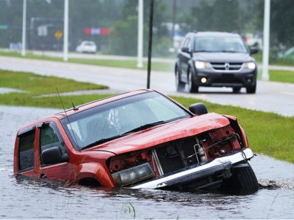 An abandoned vehicle is half submerged in a ditch next to a near flooded highway as the ou