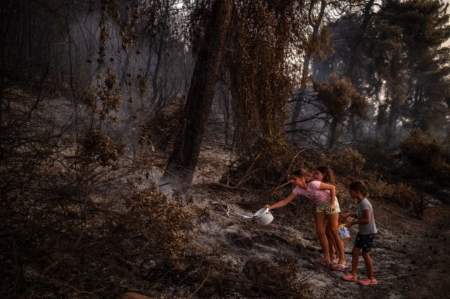 Children pour water on a smouldering fire near the village of Kastri on Evia