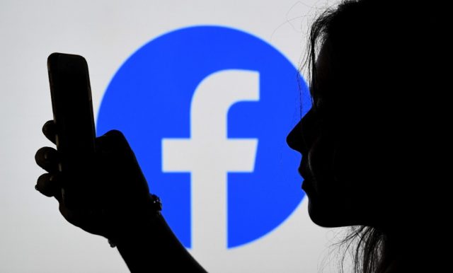 In this photo illustration, a person looks at a smart phone with a Facebook App logo displ