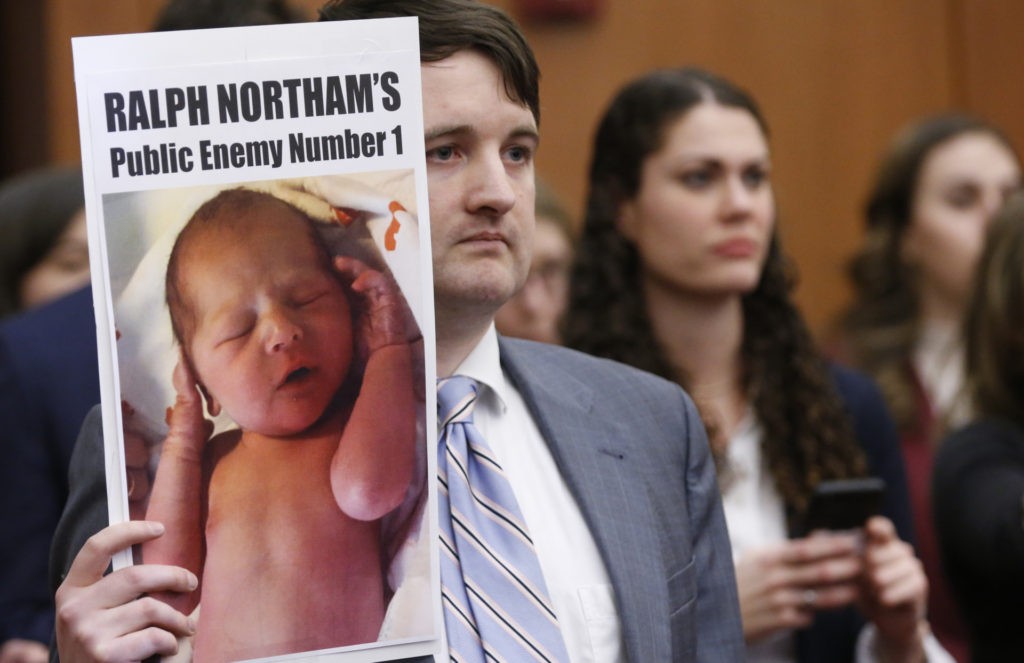 A demonstrator holds a sign as Virginia Gov. Ralph Northam, speaks during a press conference at the Capitol in Richmond, Va., Thursday, Jan. 31, 2019. Northam made a statement and answered questions about the late term abortion bill that was killed in committee. (AP Photo/Steve Helber)