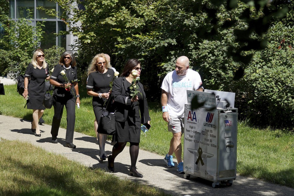 Paul Veneto, right, is joined by flight attendants as he pushes a beverage cart towards the 9/11 memorial at Logan Airport in Boston, Saturday, Aug. 21, 2021. Veneto, a former flight attendant who lost several colleagues when United Flight 175 was flown into the World Trade Center on Sept. 11, 2001, is honoring his friends on the 20th anniversary of the terrorist attacks by pushing the beverage cart from Boston to ground zero in New York. (AP Photo/Mary Schwalm)