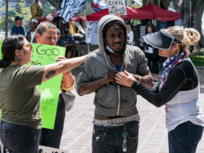 Anti-vaccine demonstrator Stacey Hidalgo, right, comforts an unidentified homeless man in a moment of prayer during an anti-vaccine rally outside City Hall in Los Angeles on Saturday, Aug. 14, 2021. The Los Angeles Police Department and local media say a man was stabbed and a reporter was attacked Saturday at …
