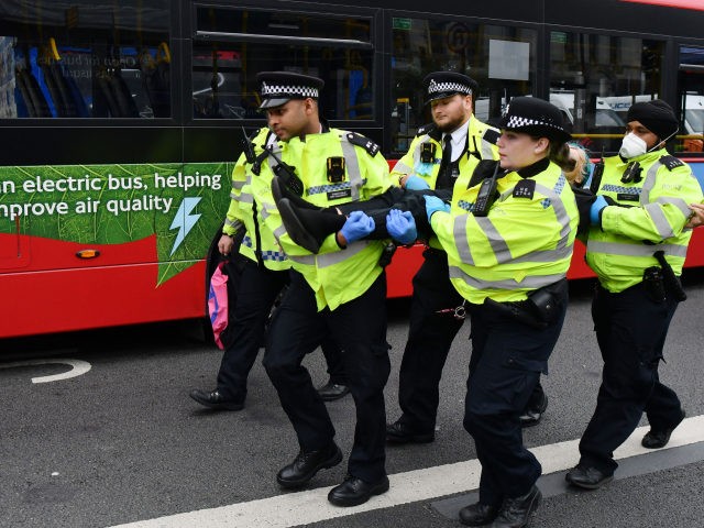 Police officers detain and escort away a climate activist from the Extinction Rebellion group blocking the road at London Bridge in central London on August 31, 2021 during the group's 'Impossible Rebellion' series of actions. - Climate change demonstrators from environmental activist group Extinction Rebellion continued with their latest round …