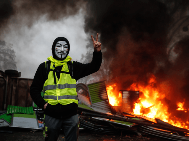 TOPSHOT - A protester wearing a Guy Fawkes mask makes the victory sign near a burning barricade during a protest of Yellow vests (Gilets jaunes) against rising oil prices and living costs, on December 1, 2018 in Paris. (Photo by Abdulmonam EASSA / AFP) (Photo by ABDULMONAM EASSA/AFP via Getty …