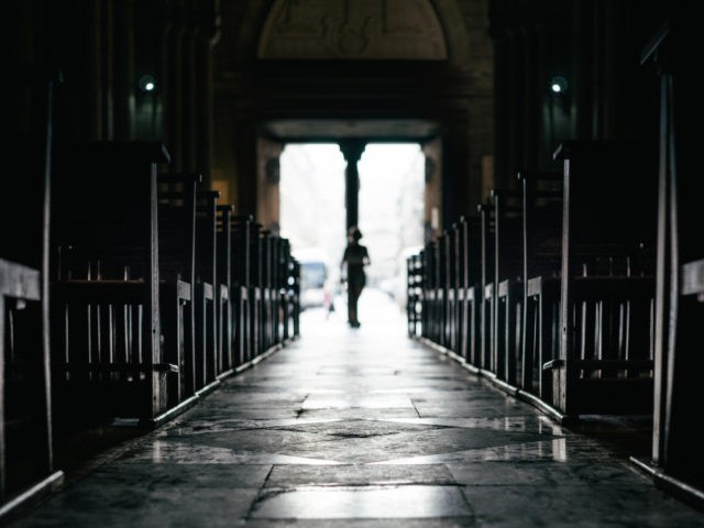 Rows of bench inside a silent church with passerby moving in from exit