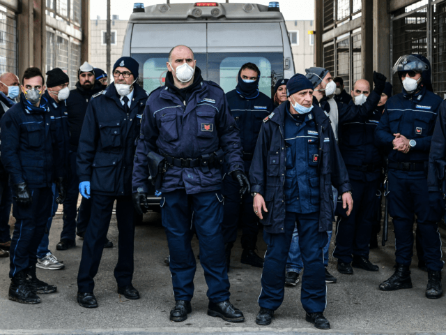 Prison Police officers stand guard after an ambulance (Rear) entered the SantAnna prison during a protest of inmates' relatives in Modena, Emilia-Romagna, in one of Italy's quarantine red zones on March 9, 2020. - Inmates in four Italian prisons have revolted over new rules introduced to contain the coronavirus outbreak, …