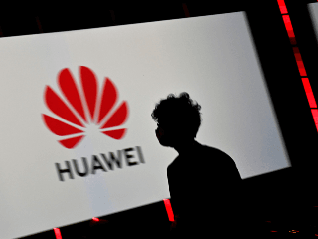 A visitor with a face mask walks past the logo of Huawei displayed on a screen during the Internationale Funkausstellung IFA international trade show for consumer electronics and home appliances on September 3, 2020 at the fair grounds in Berlin. - A special edition of the fair, adapted to health …