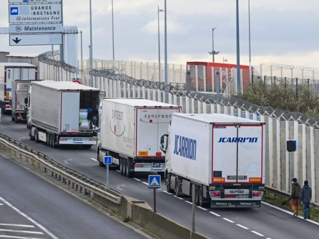 Migrants walk to climb into the back of lorries bound for Britain while traffic is stopped