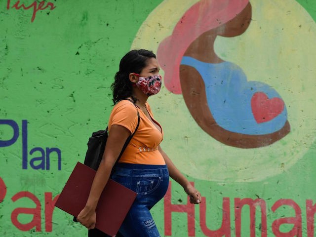 A pregnant woman wearing a face mask walks past a mural "Humanized birth plan" i