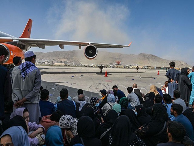 TOPSHOT - Afghan people sit as they wait to leave the Kabul airport in Kabul on August 16, 2021, after a stunningly swift end to Afghanistan's 20-year war, as thousands of people mobbed the city's airport trying to flee the group's feared hardline brand of Islamist rule. (Photo by Wakil Kohsar / AFP) (Photo by WAKIL KOHSAR/AFP via Getty Images)