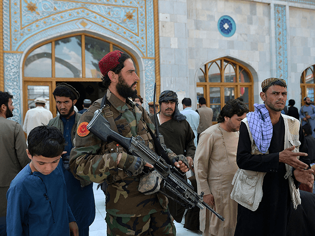 An armed Taliban fighter stands guard as Muslim devotees leave after Friday prayers at the