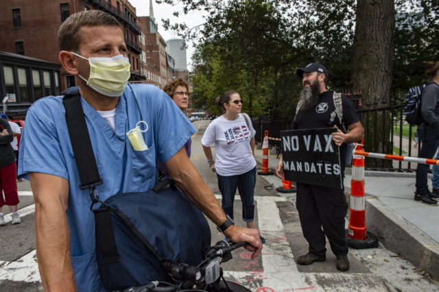 A nurse from Brigham and Women's Hospital watches as demonstrators gather outside the Massachusetts State House in Boston to protest Covid-19 vaccination and mask mandates. (Photo by JOSEPH PREZIOSO / AFP) (Photo by JOSEPH PREZIOSO/AFP via Getty Images)