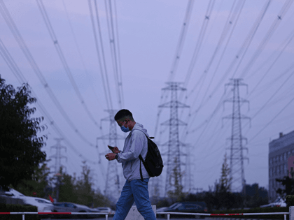 A man walks below power lines in Beijing on September 28, 2021. (Photo by LEO RAMIREZ/AFP
