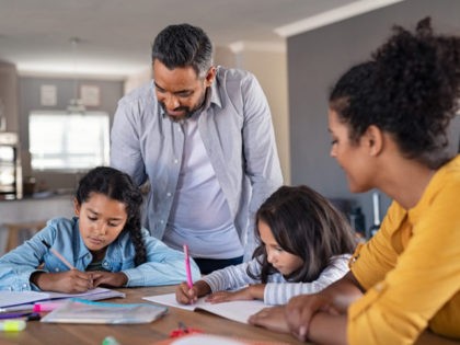 Indian parents helping children with their homework at home. Middle eastern father and african mother helping daughters studying at home. Little girls completing their exercises with the help of dad and mom, homeschooling concept.