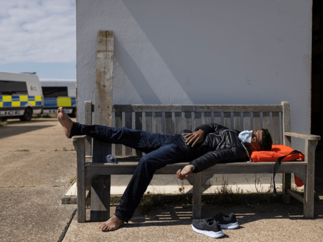 DUNGENESS, ENGLAND - AUGUST 04: A man lays on a bench as a group of around 40 migrants arr